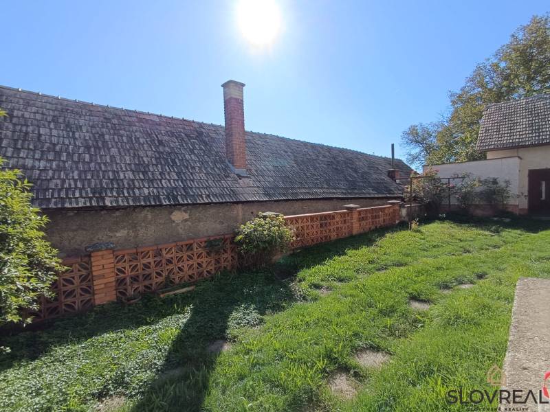 : Predaj rodinného domu s veľkým pozemkom v obci Pitelová  - Rodinný dom v Pitelovej so záhradou, tehlovým plotom a šikmou strechou.