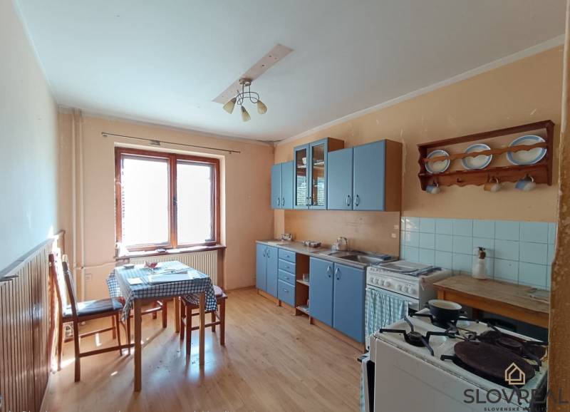 : Predaj rodinného domu s veľkým pozemkom v obci Pitelová  - Tradičná kuchyňa s modrou linkou, drevenou dekorom podlahy a jedálenským stolom.