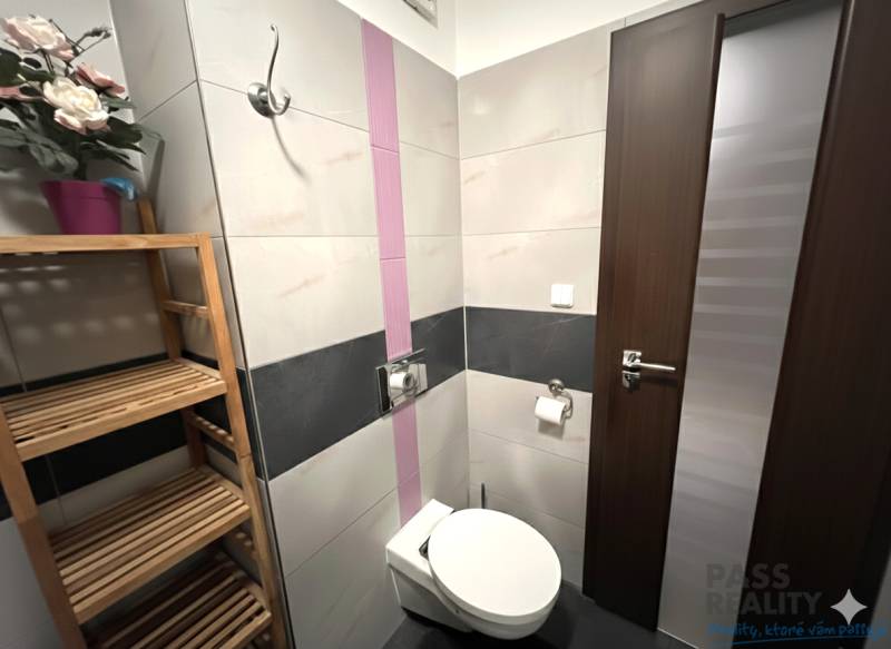 REZERVOVANÉ-PREDAJ 2 izbový byt s garážou v skvelej lokalite v Ružinov - Kúpeľňa v 2-izbovom byte s toaletou, dreveným regálom a dekoratívnymi kvetmi.