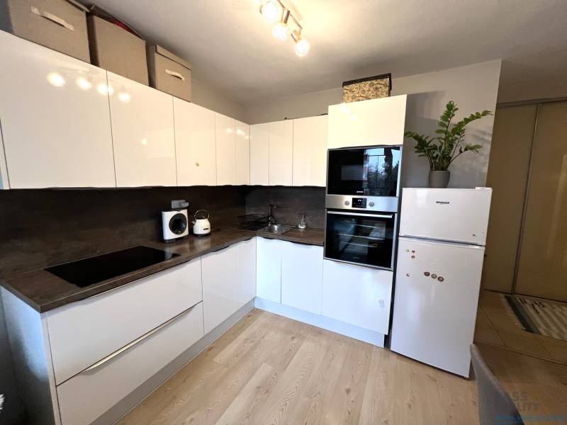 REZERVOVANÉ-PREDAJ 2 izbový byt s garážou v skvelej lokalite v Ružinov - Kuchyňa v 2-izbovom byte s bielymi skrinkami, spotrebičmi a podlahou s dreveným dekorom.