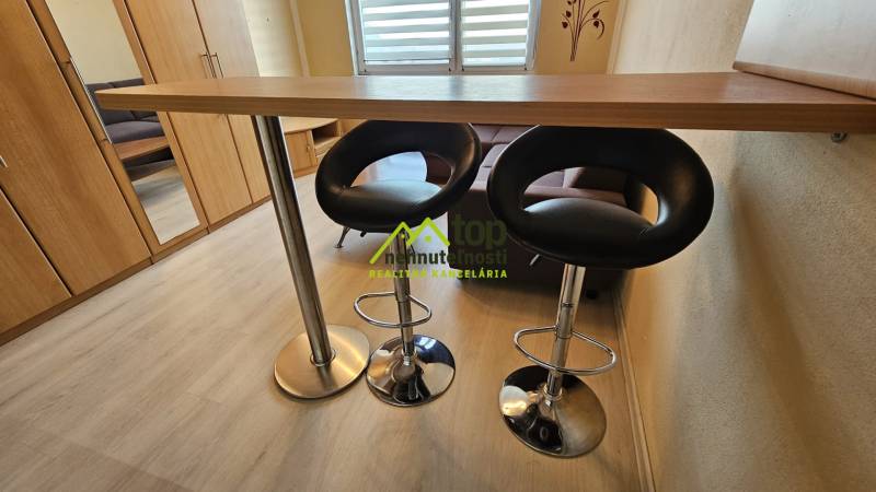 TOPOĽĆANY - zariadená garsónka na sídlisku JUH - Garsónka s pultom, stoličkami a podlahou s dreveným dekorom.