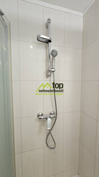 TOPOĽĆANY - zariadená garsónka na sídlisku JUH - Sprchový kút v garsónke s bielymi obkladačkami a chrómovou sprchovou batériou.