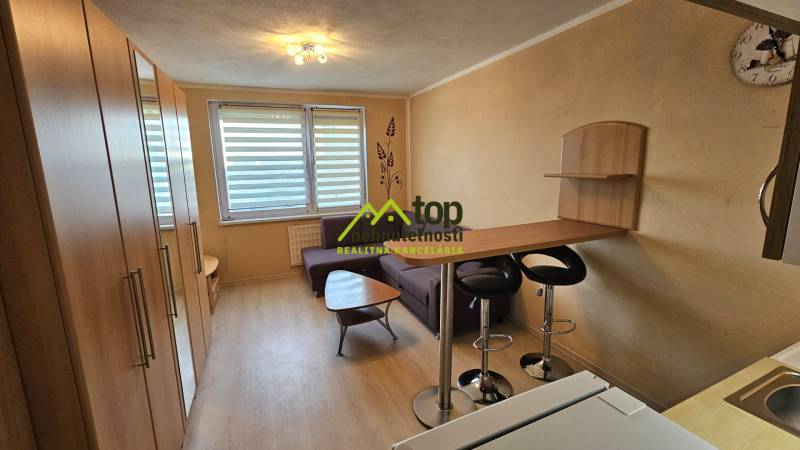 TOPOĽĆANY - zariadená garsónka na sídlisku JUH - Garsónka s podlahou s dreveným dekorom, kuchynským pultom a sedačkou.