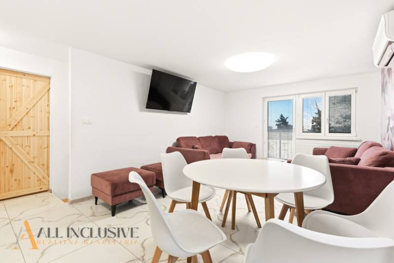 NADŠTANDARDNÁ REKREAČNÁ CHATA | DUCHONKA  - Obývačka chaty s bielym jedálenským stolom, pohovkami a televízorom na stene.