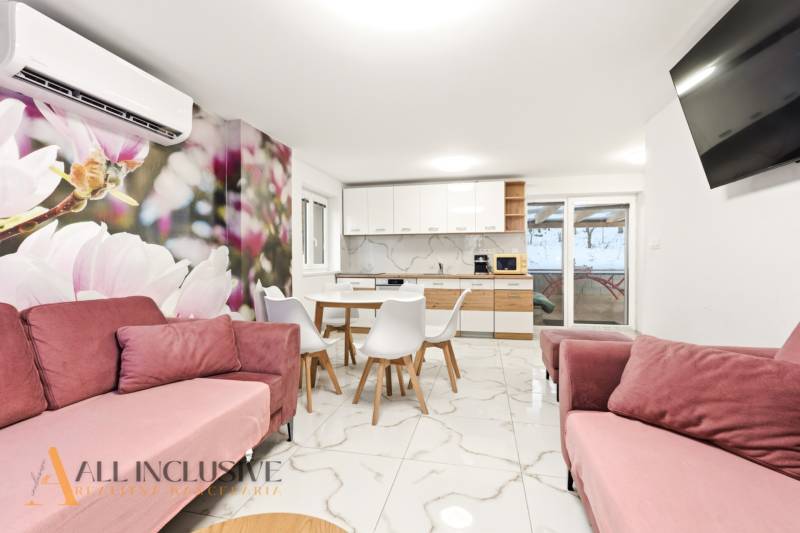 NADŠTANDARDNÁ REKREAČNÁ CHATA | DUCHONKA  - Chata interiér s kvetinovou tapetou, kuchyňou, ružovými sedačkami a jedálenskými stoličkami.