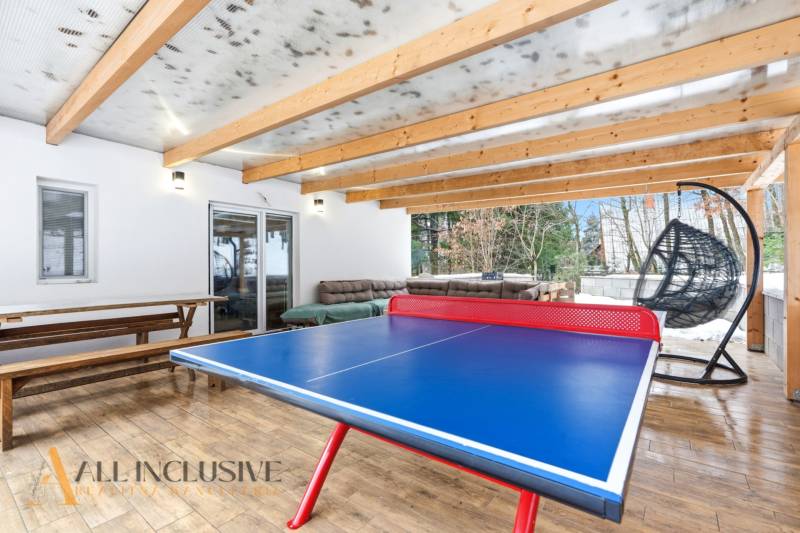 NADŠTANDARDNÁ REKREAČNÁ CHATA | DUCHONKA  - Pingpongový stôl vedľa lavice a hojdačky na terase v chate s dreveným dekorom.