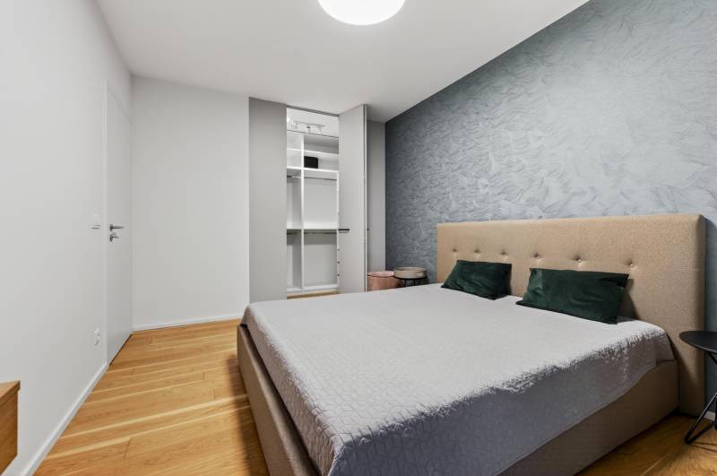 ︱ PREDAJ Nadštandardný 3-izb. byt v projekte Gansberg Koliba - Spálňa s vstavanou skriňou, čalúnenou posteľou a podlahou s dreveným dekorom v 3-izbovom byte.