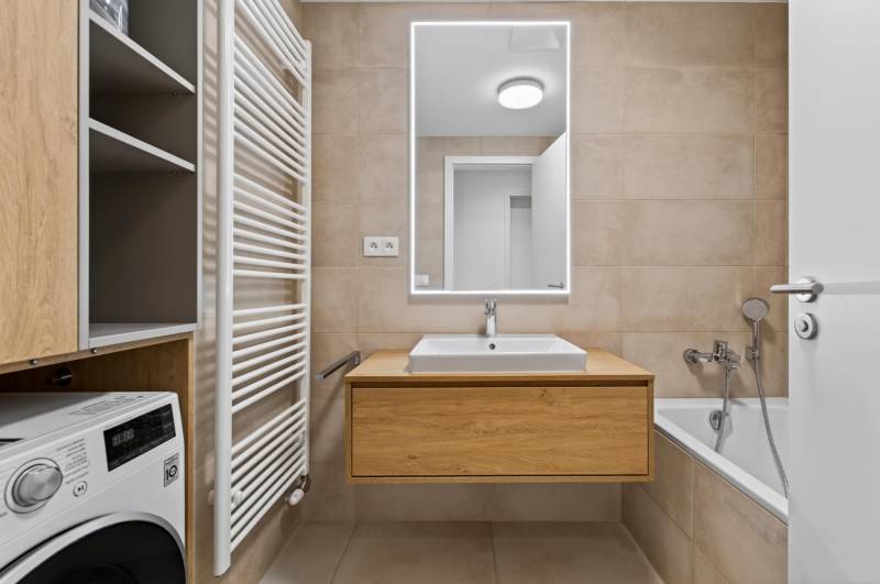 ︱ PREDAJ Nadštandardný 3-izb. byt v projekte Gansberg Koliba - Kúpeľňa s vaňou, umývadlom, zrkadlom a skrinkou v 3-izbovom byte.