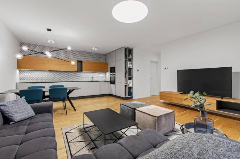 ︱ PREDAJ Nadštandardný 3-izb. byt v projekte Gansberg Koliba - Obývacia izba s kuchyňou v 3-izbovom byte, podlaha s dreveným dekorom, moderný nábytok.