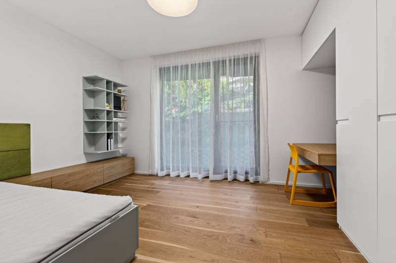 ︱ PREDAJ Nadštandardný 3-izb. byt v projekte Gansberg Koliba - Izba s podlahou s dreveným dekorom, stolík so žltou stoličkou, posteľ, polička.