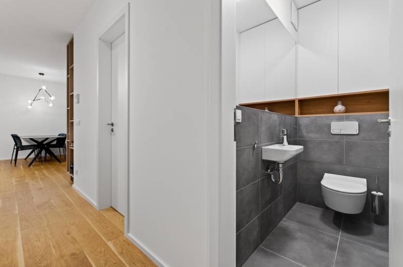 ︱ PREDAJ Nadštandardný 3-izb. byt v projekte Gansberg Koliba - V 3-izbovom byte sa nachádza toaleta s sivými obkladmi a podlaha s dreveným dekorom.