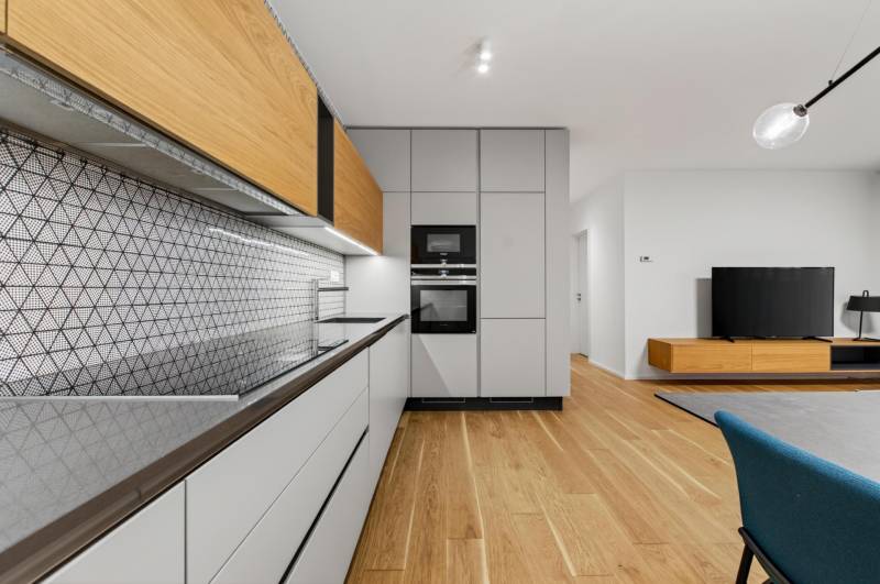 ︱ PREDAJ Nadštandardný 3-izb. byt v projekte Gansberg Koliba - Kuchyňa v 3-izbovom byte s geometrickým obkladom a podlahou s dreveným dekorom.