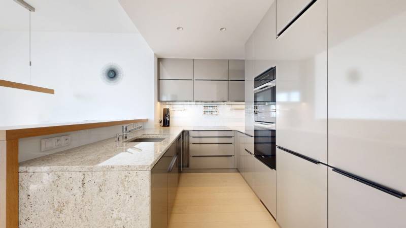 Elegantný byt na mieru s panorámou hradu  - Kuchyňa v 3-izbovom byte s lesklými skrinkami, mramorovou doskou a podlahou s dreveným dekorom.