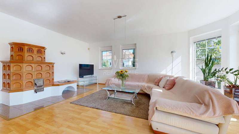 RIVERS - Veľkorysý rodinný dom po rekonštrukcii  - Obývacia izba v rodinnom dome s kachľovou pecou, rohovou sedačkou a podlahou s dreveným dekorom.