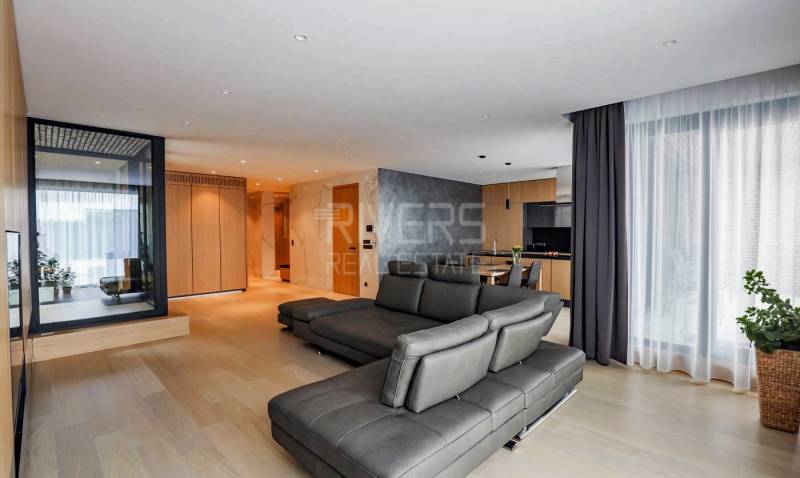 RIVERS I Prémiový 4-izbový byt s panoramatickým výhľadom na mesto - Obývacia izba v 4-izbovom byte s podlahou s dreveným dekorom a koženou sedačkou.