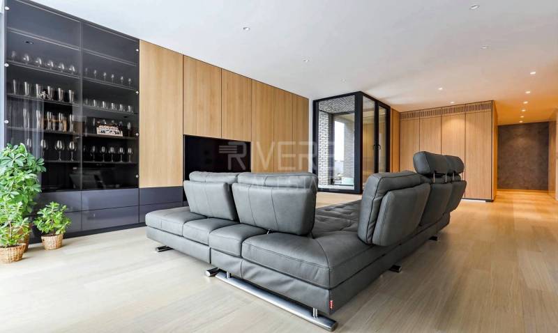 RIVERS I Prémiový 4-izbový byt s panoramatickým výhľadom na mesto - Obývacia izba v 4-izbovom byte s podlahou s dreveným dekorom a šedou sedačkou.