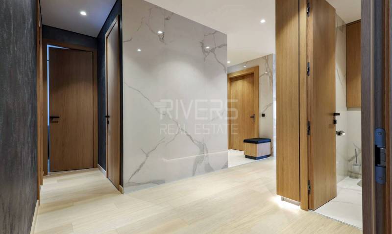 RIVERS I Prémiový 4-izbový byt s panoramatickým výhľadom na mesto - Chodba so stenou s mramorovým vzorom, drevenými dverami a podlahou s dreveným dekorom.