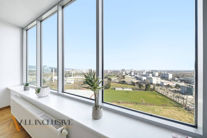 Na predaj luxusný 2-izb. byt s loggiou v Bratislave  - Výhľad z 2-izbového bytu s veľkými oknami, izbové rastliny, podlaha s dreveným dekorom.