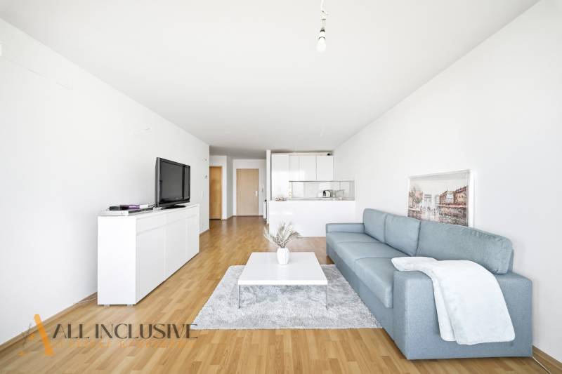 Na predaj luxusný 2-izb. byt s loggiou v Bratislave  - Obývačka s modrou pohovkou, bielym nábytkom a podlahou s dreveným dekorom v 2-izbovom byte.