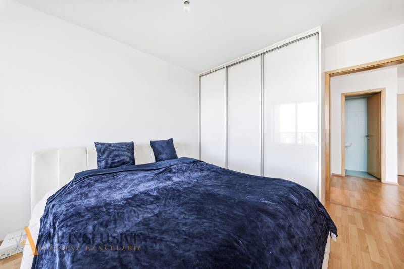 Na predaj luxusný 2-izb. byt s loggiou v Bratislave  - Spálňa v 2-izbovom byte s posteľou, šatníkom a podlahou s dreveným dekorom.