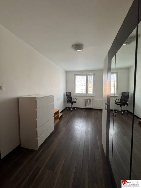 Prenájom 2-izb bytu v Bratislave-Rača - Svetlá izba s podlahou s dreveným dekorom, skriňou a kreslom v 2-izbovom byte.