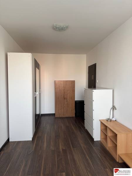 Prenájom 2-izb bytu v Bratislave-Rača - Miestnosť v 2-izbovom byte s podlahou s dreveným dekorom, bielymi skriňami a nábytkom.