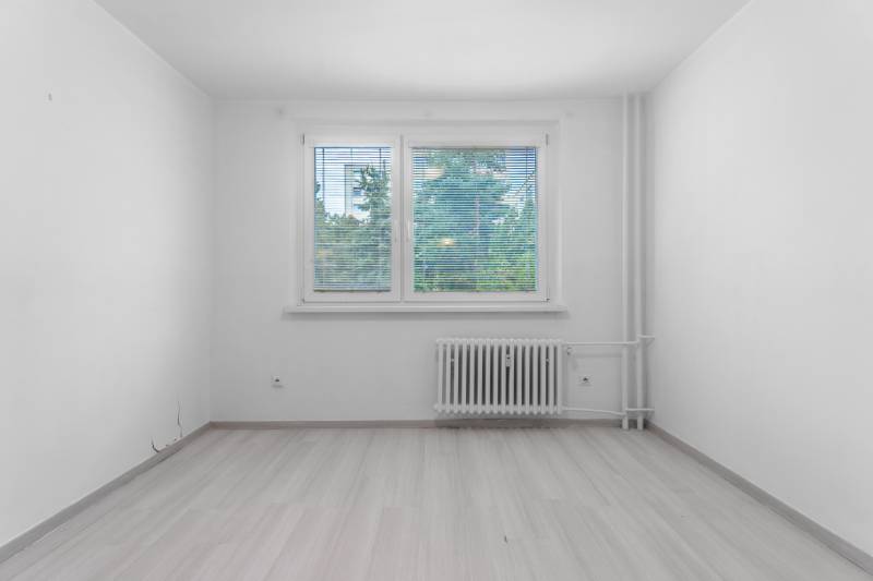 I Predaj 3- izbového bytu v Dúbravke - Izba v 3-izbovom byte s podlahou s dreveným dekorom a radiátorom pod oknom.