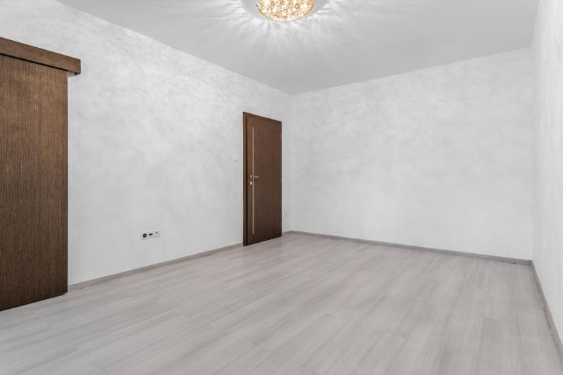 I Predaj 3- izbového bytu v Dúbravke - Izba s dverami a podlahou s dreveným dekorom v 3-izbovom byte.