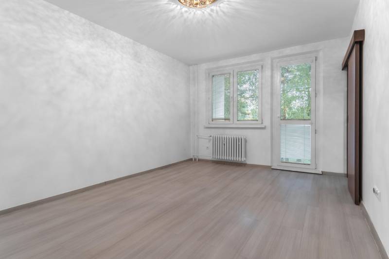 I Predaj 3- izbového bytu v Dúbravke - Izba v 3-izbovom byte s podlahou s dreveným dekorom a veľkými oknami.