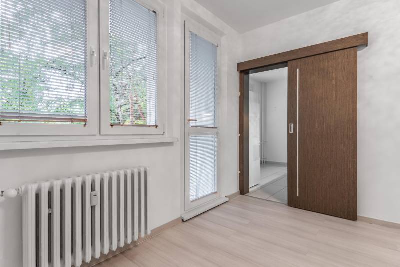 I Predaj 3- izbového bytu v Dúbravke - Interiér 3-izbového bytu s radiátorom, žalúziami a podlahou s dreveným dekorom.