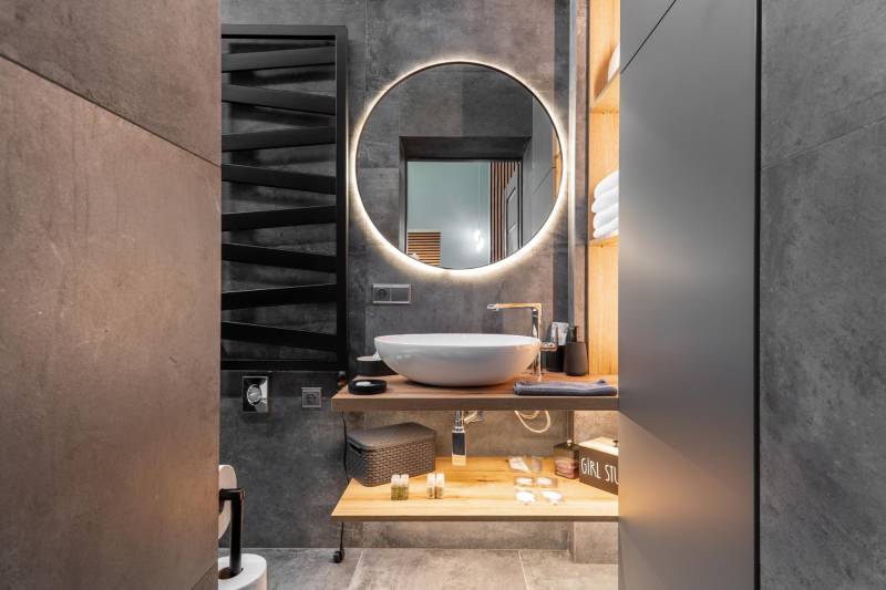 | Luxusný dvojúrovňový mezonet v Starom Meste - Kúpeľňa v 3-izbovom byte s okrúhlym zrkadlom a umývadlom na drevenej doske.