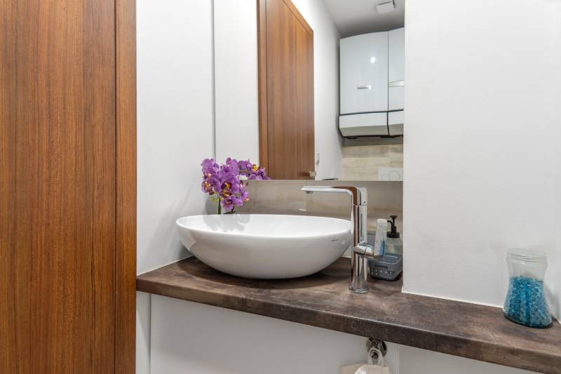 I Luxusný byt v historickom centre Bratislavy - Kompaktná kúpeľňa s bielym umývadlom, drevený dekor, fialové kvety. 2-izbový byt.