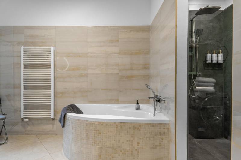 I Luxusný byt v historickom centre Bratislavy - Kúpeľňa v 2-izbovom byte s rohovou vaňou, obkladanými stenami a sprchovým kútom.