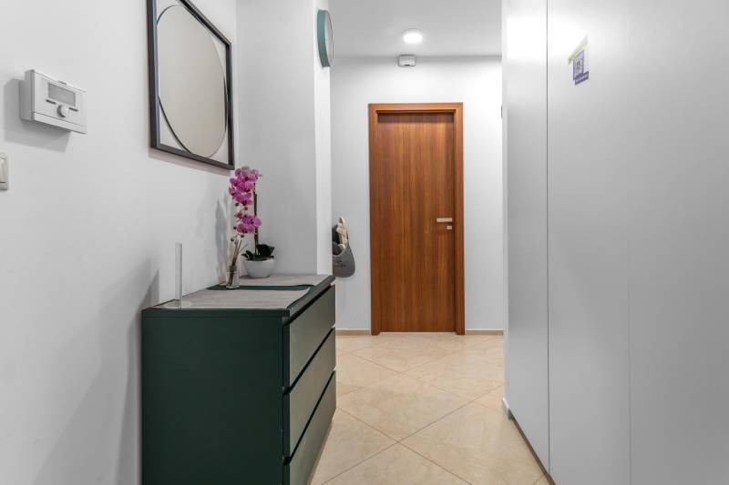 I Luxusný byt v historickom centre Bratislavy - Chodba v 2-izbovom byte s kvetom, zrkadlom a drevenými dverami.