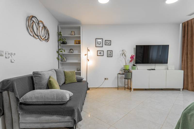 I Luxusný byt v historickom centre Bratislavy - Obývačka v 2-izbovom byte s TV, pohovkou a minimalistickou dekoráciou na bielej stene.