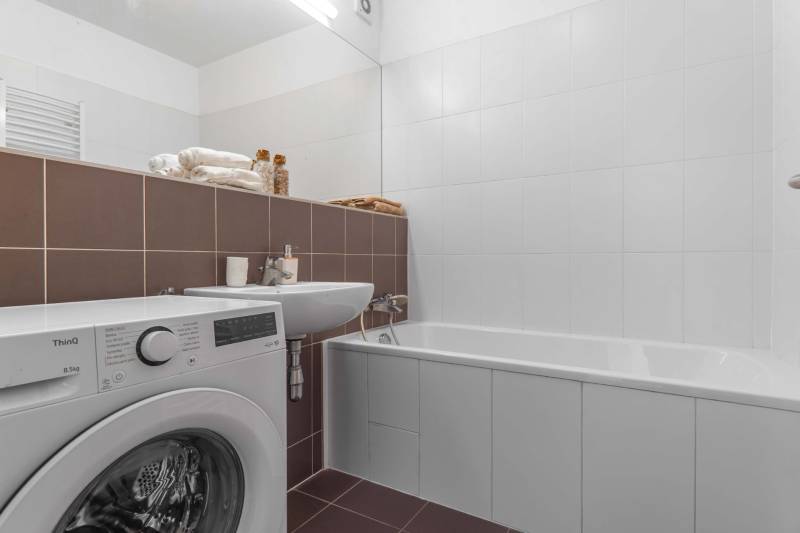 I na predaj 2i byt v komplexe Tri Veže na Bajkalskej - Kúpeľňa v 2-izbovom byte s práčkou, vaňou a umývadlom, vybavená bielymi a hnedými obkladmi.