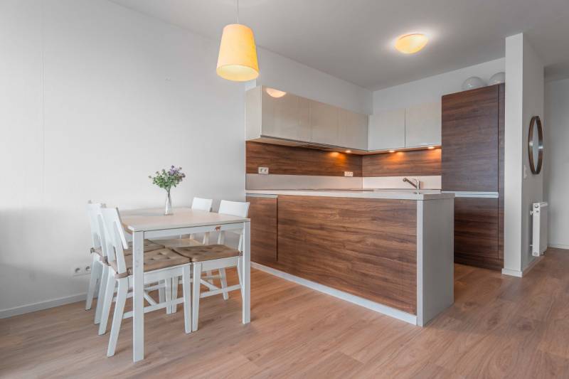 I na predaj 2i byt v komplexe Tri Veže na Bajkalskej - Kuchyňa v 2-izbovom byte s dreveným dekorom a bielym jedálenským stolom.