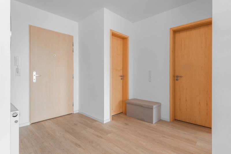 I na predaj 2i byt v komplexe Tri Veže na Bajkalskej - Interiér 2-izbového bytu s podlahou s dreveným dekorom, troma dverami a lavicou.