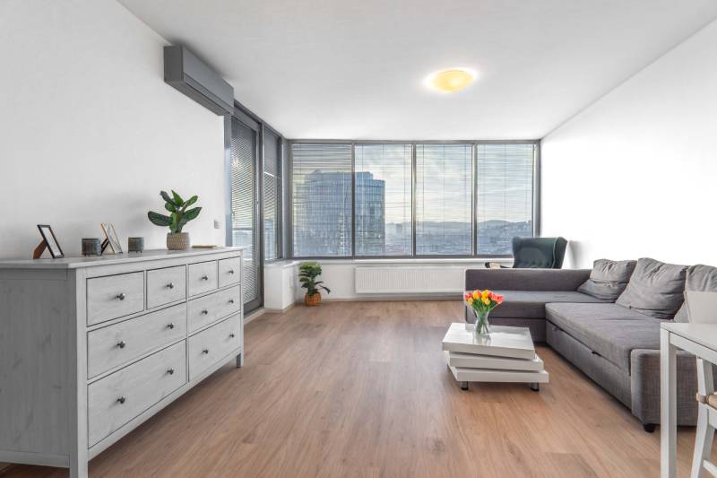 I na predaj 2i byt v komplexe Tri Veže na Bajkalskej - Obývačka v 2-izbovom byte s pohovkou a podlahou s dreveným dekorom, svetlý priestor.