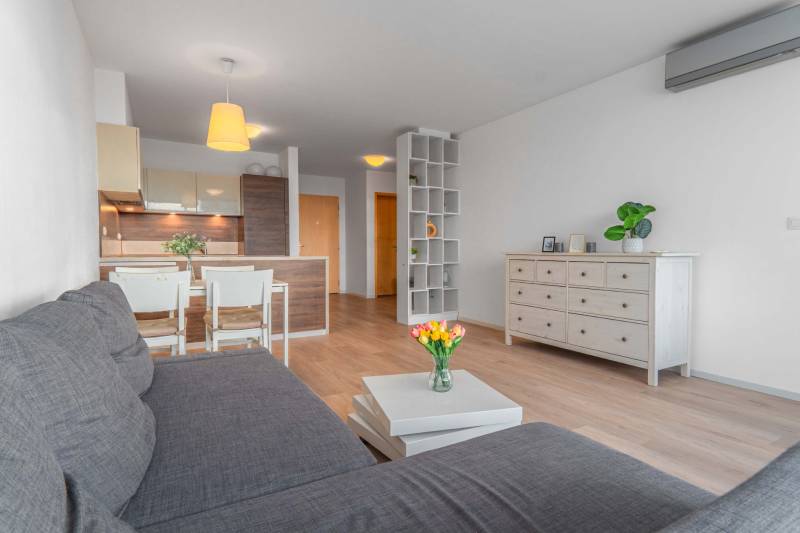 I na predaj 2i byt v komplexe Tri Veže na Bajkalskej - Obývačka s podlahou s dreveným dekorom a kuchynským kútom v 2-izbovom byte.