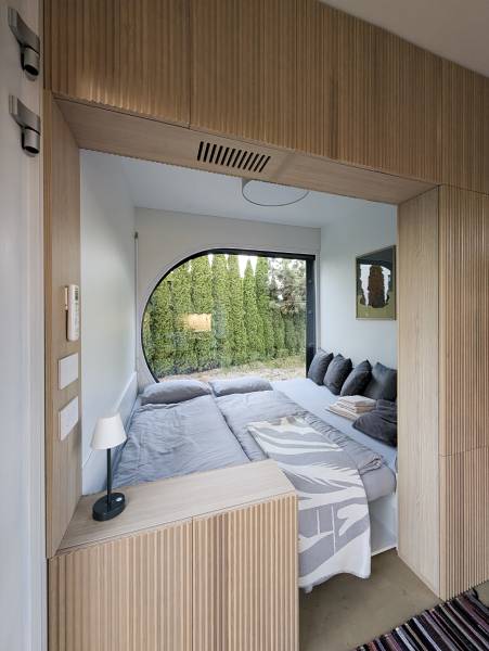 I Predaj Ecocapsule – autonómne ekologické bývanie - Spálňa so vstavanou posteľou, okrúhlym oknom a podlahou s dreveným dekorom.