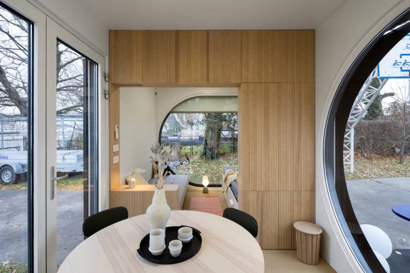 I Predaj Ecocapsule – autonómne ekologické bývanie - Sklenené dvere, drevené dekorácie, okrúhle okno a stôl s nádobami v jedálenskej časti.