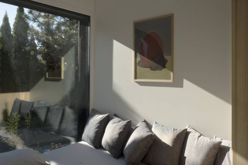 I Predaj Ecocapsule – autonómne ekologické bývanie - Interiér so sivými vankúšmi, obrazom na stene a výhľadom do záhrady.