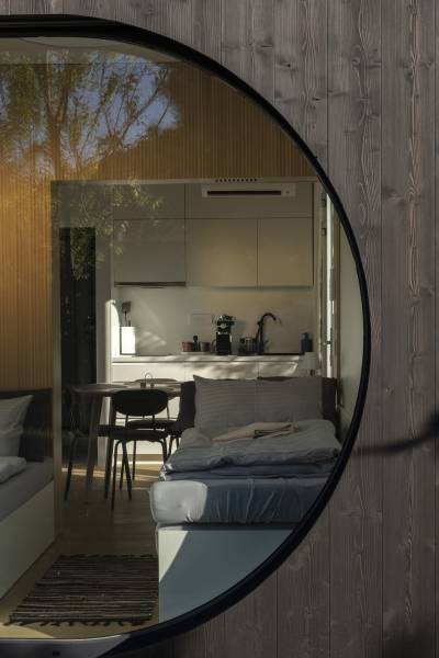 I Predaj Ecocapsule – autonómne ekologické bývanie - Interiér cez okrúhle okno, zvýrazňujúci Zvláštne nehnuteľnosti s kuchynským kútom a pohovkou.