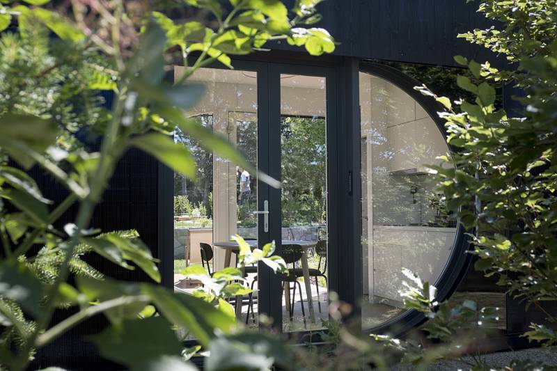 I Predaj Ecocapsule – autonómne ekologické bývanie - Sklenené dvere a kruhové okno medzi zeleňou pri zvláštnych nehnuteľnostiach v Bratislave.