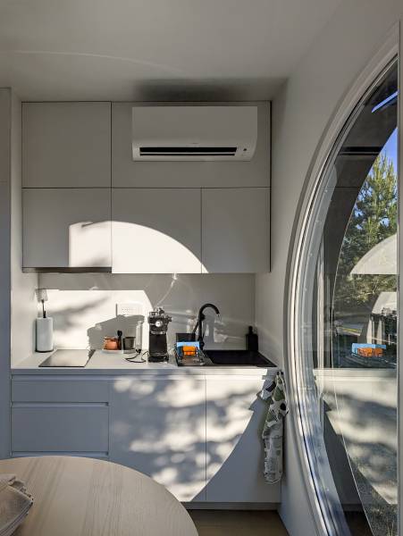 I Predaj Ecocapsule – autonómne ekologické bývanie - Kuchynská časť Zvláštnych nehnuteľností s bielou linkou, oblúkovým oknom a klimatizáciou.