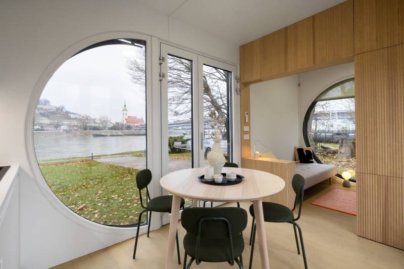 I Predaj Ecocapsule – autonómne ekologické bývanie - Kruhové okná v interiéri s výhľadom na rieku a architektúru Zvláštnych nehnuteľností.