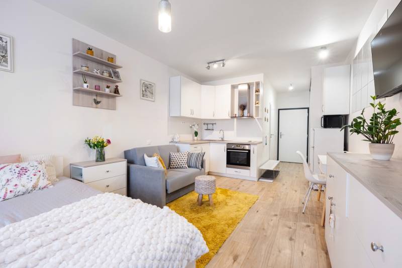 Prenájom 1-izbového bytu, Béžová, Béžová, Petržalka - REZERVOVANÉ - Svetlý interiér 1-izbového bytu s kuchyňou, posteľou a podlahou s dreveným dekorom.