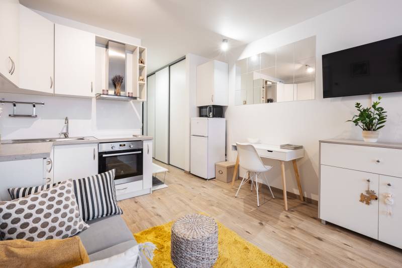 Prenájom 1-izbového bytu, Béžová, Béžová, Petržalka - REZERVOVANÉ - Obývacia izba 1-izbového bytu s kuchynskou linkou, bielym nábytkom a podlahou s dreveným dekorom.