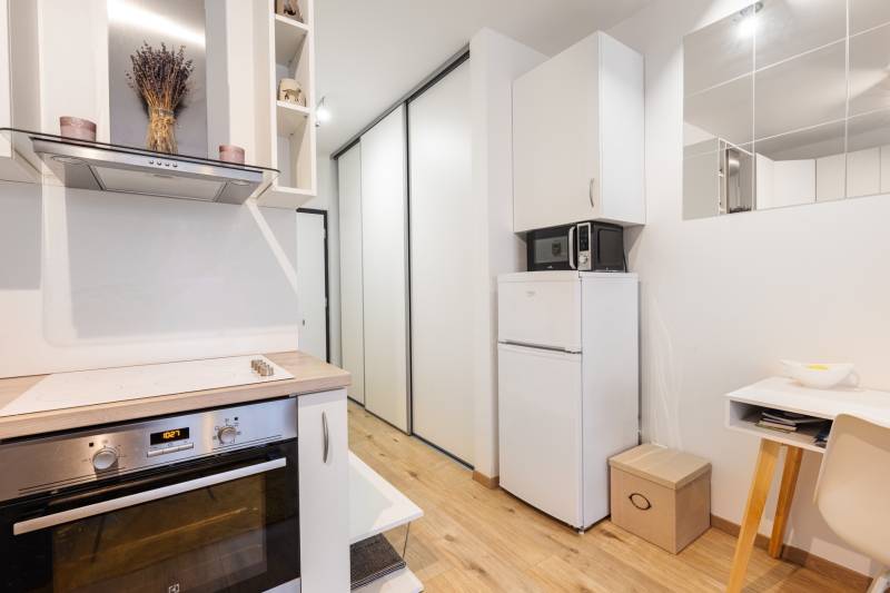 Prenájom 1-izbového bytu, Béžová, Béžová, Petržalka - REZERVOVANÉ - Kompaktná kuchyňa s varnou doskou, chladničkou a podlahou s dreveným dekorom v 1-izbovom byte.